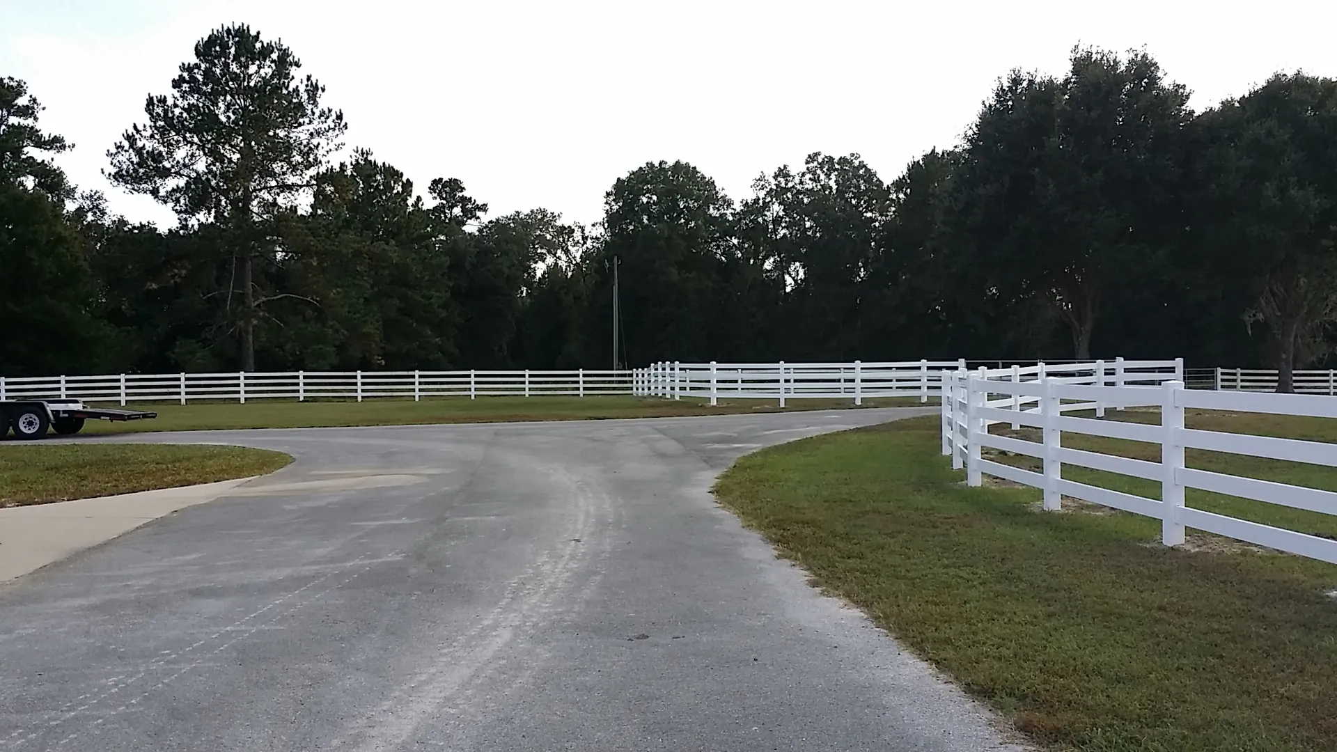 White vinyl ranch rail fence lining a tree-lined driveway at a rural Florida property