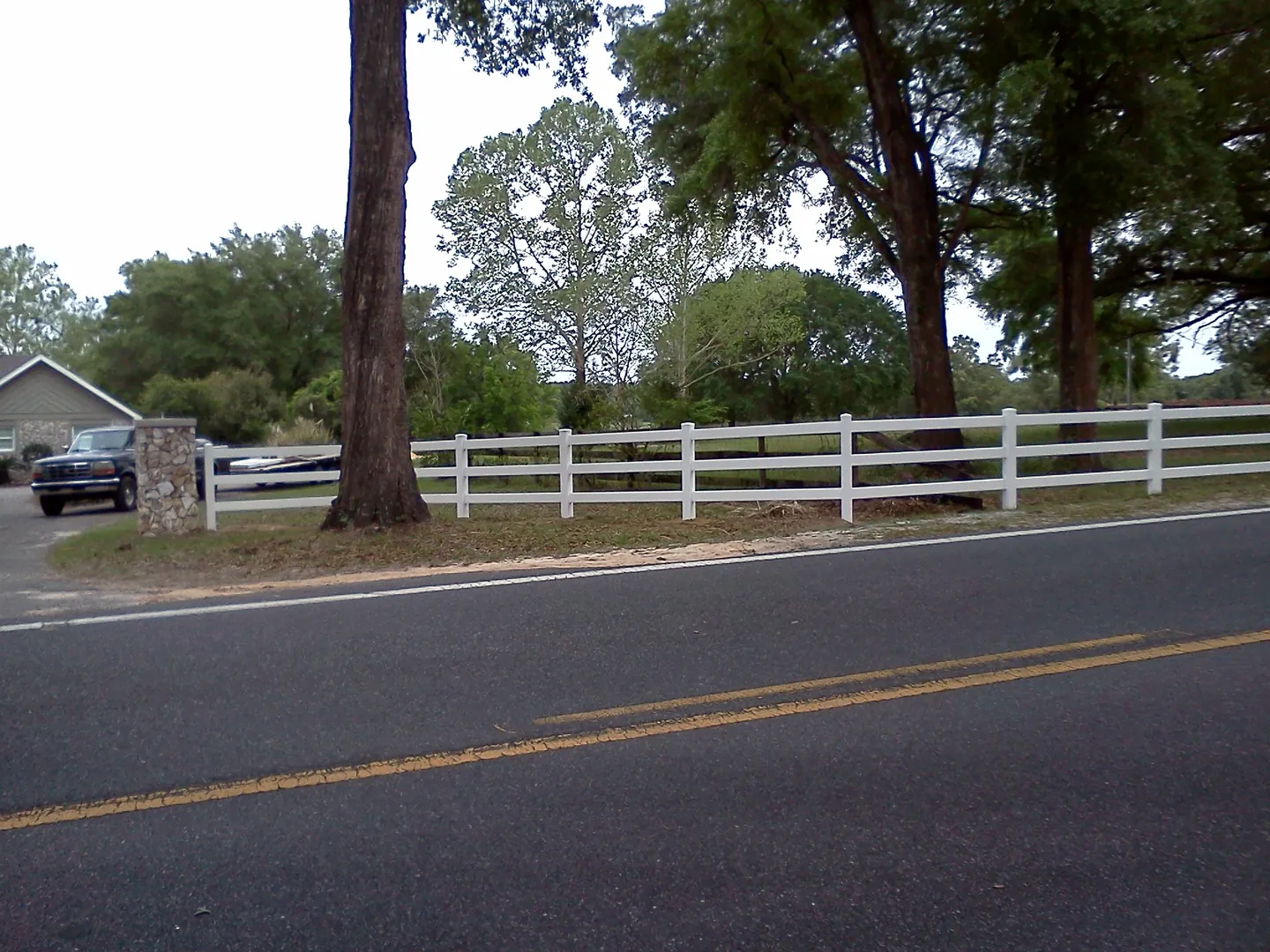 White vinyl ranch rail fence running along a rural road surrounded by trees in Florida