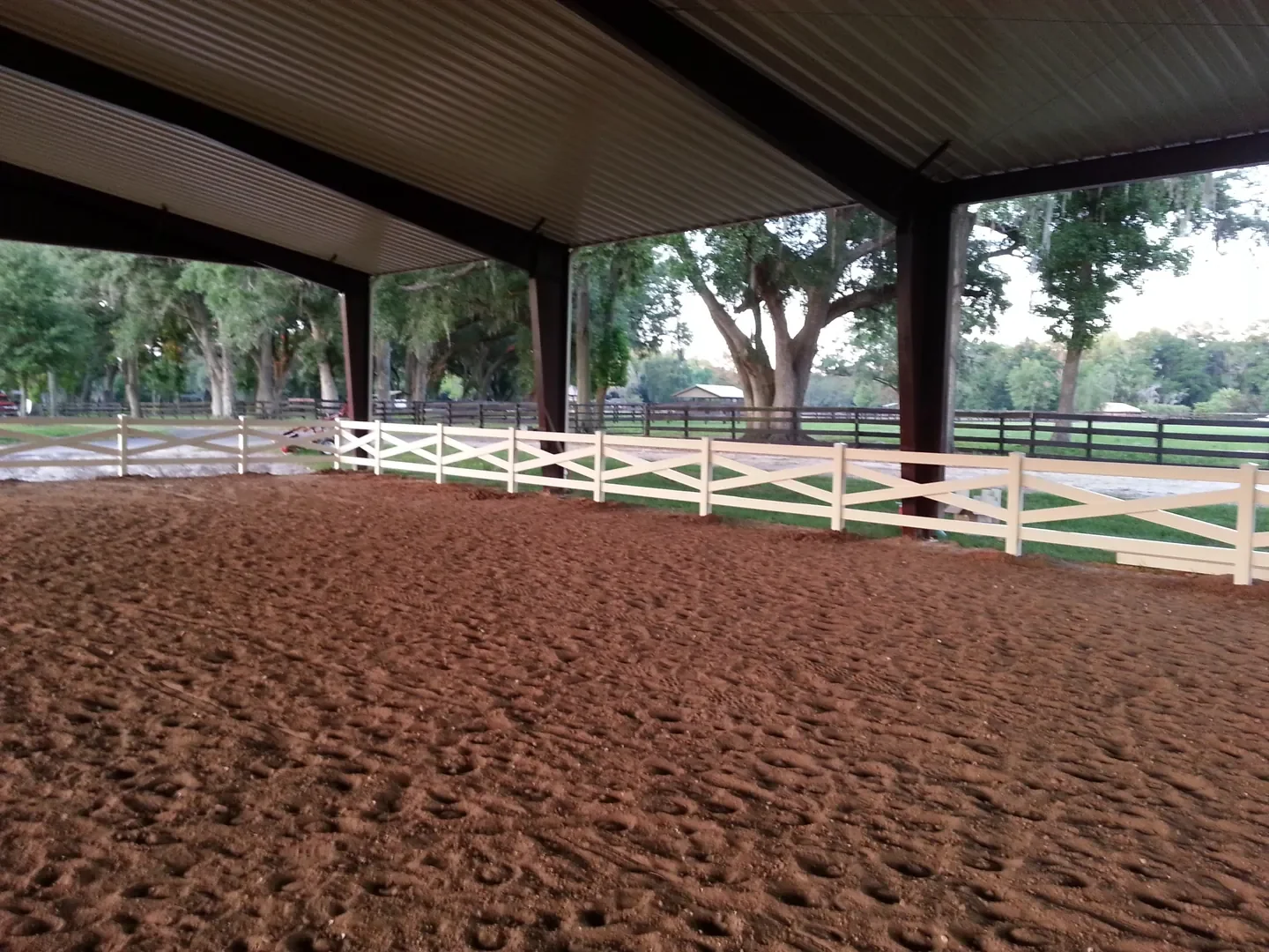White vinyl arena fencing inside a covered equestrian riding arena at a Florida horse property